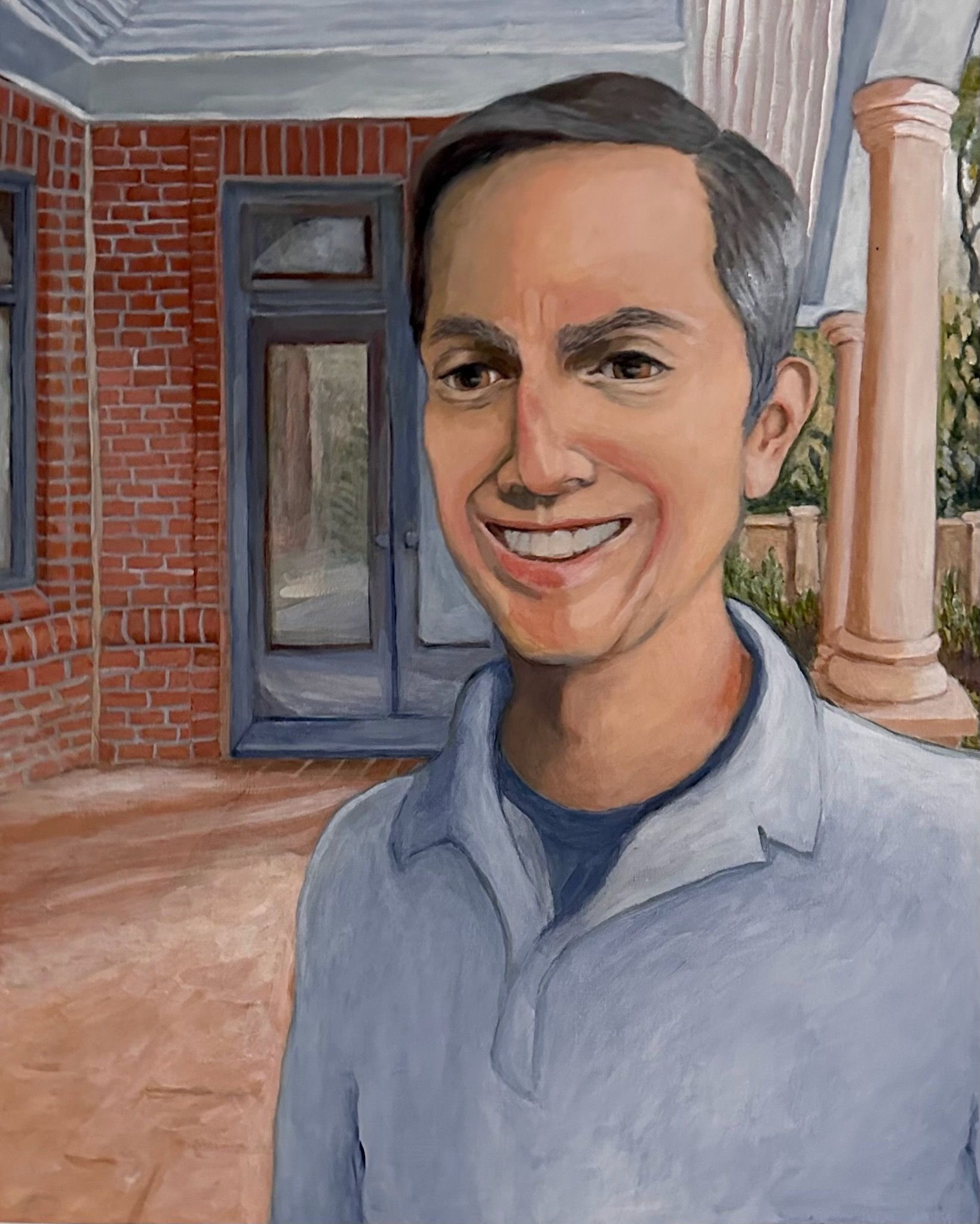 Smiling man in a blue polo stands on a porch beside brick walls and white columns.