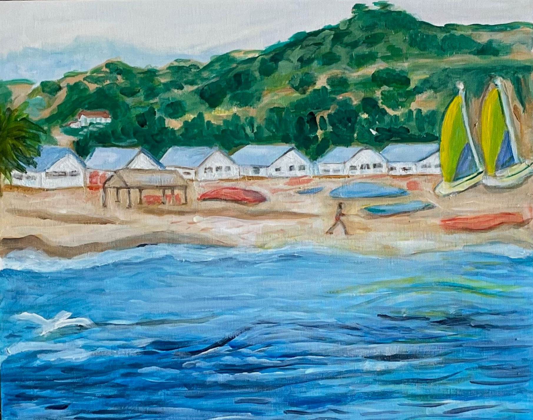 Colorful seaside village with sailboats, white houses, sandy beach, green hills, and blue water.