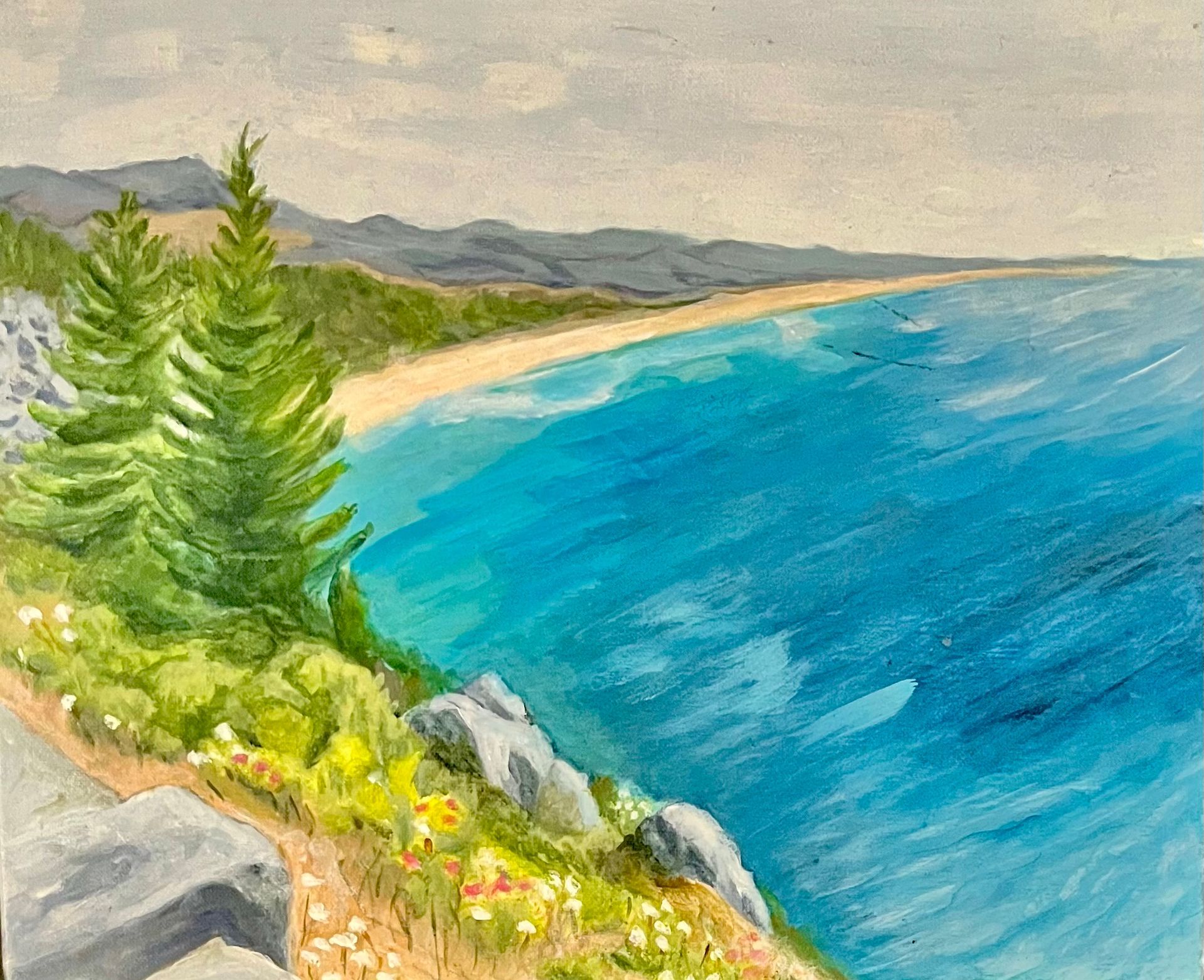 Coastal cliff path with pine trees, rocky shore, distant mountains, and bright blue sea
