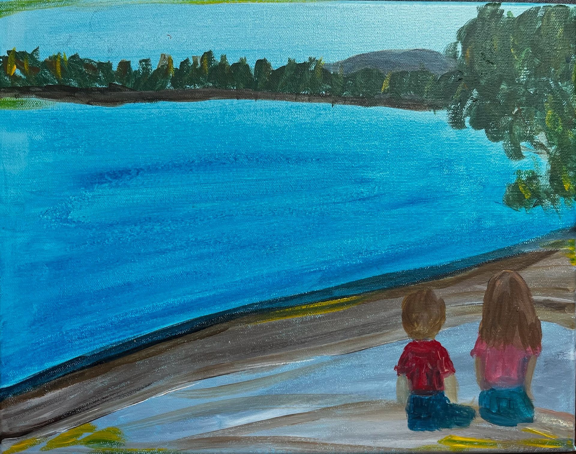 Two children sit by a blue lake, looking across the water toward a tree-lined shore.