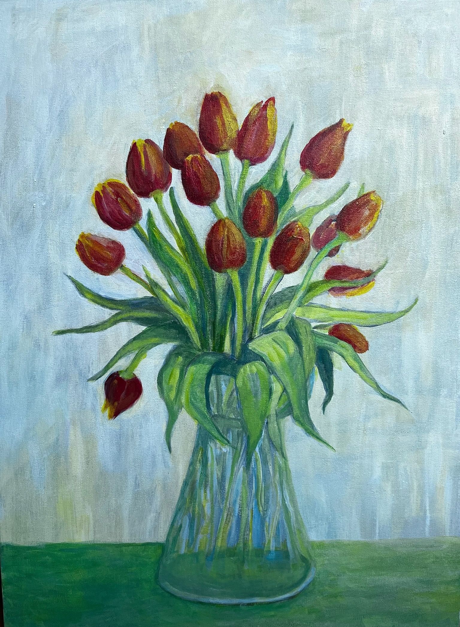 A vase of red tulips with green leaves on a green surface against a pale blue background