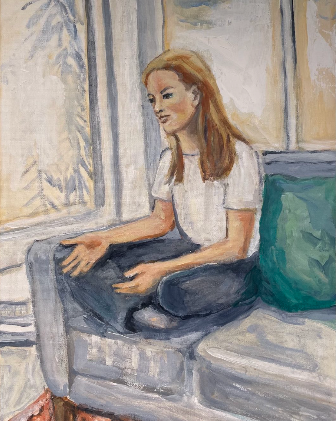 Person sitting cross-legged on a couch by a window, holding a tablet with a teal pillow beside them