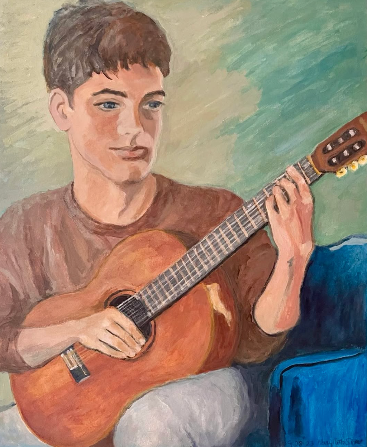 Young person playing an acoustic guitar on a blue couch, with a green and beige painted background.
