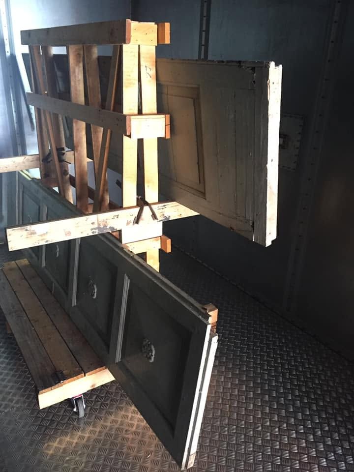 Espositore in legno con due pannelli dalla cornice scura, illuminato dalla luce del sole su un pavimento in metallo.