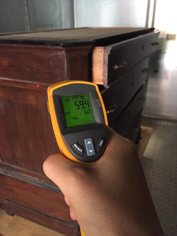 Mano che regge un termometro a infrarossi giallo puntato verso un cassettone di legno in una stanza
