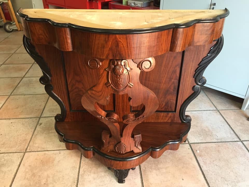 Tavolino laterale in legno intagliato con piano in marmo color crema e gambe scolpite, su un pavimento piastrellato