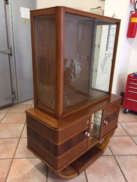 Mobiletto in legno marrone su un pavimento piastrellato, con una vetrina in vetro e una piccola anta aperta nella parte inferiore.