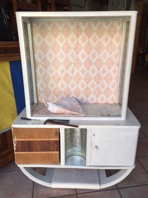 Vetrina bianca aperta con pannello posteriore decorato, un cassetto e ripiani con tessuti piegati e libri.