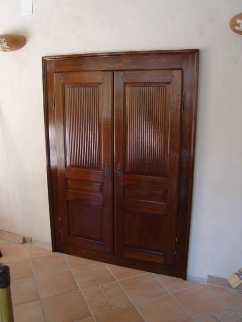 Doppia porta in legno con pannelli intagliati, appoggiata a una parete bianca su un pavimento piastrellato