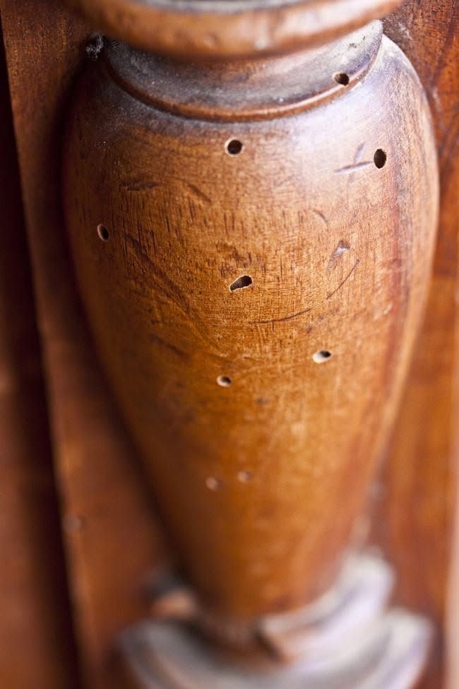 Primo piano di una gamba di mobile in legno intagliato, con finitura marrone calda e piccoli fori