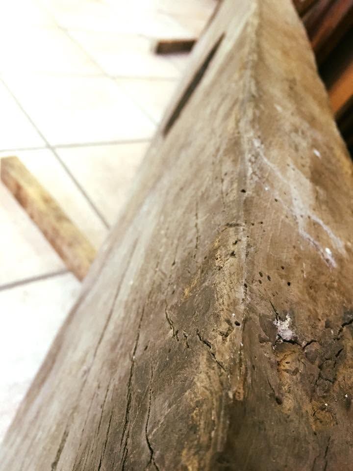 Primo piano di una trave di legno consumata, con una superficie screpolata e ruvida, su un pavimento piastrellato.