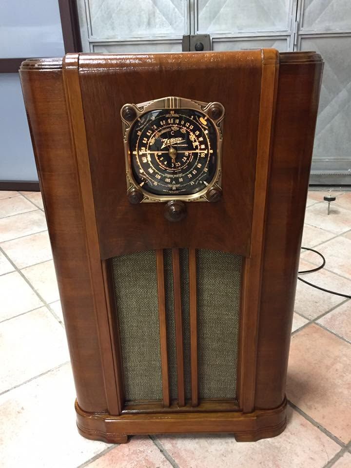 Mobile radio vintage in legno con quadrante rotondo e griglia dell’altoparlante sul davanti, appoggiata su un pavimento piastrellato all’interno
