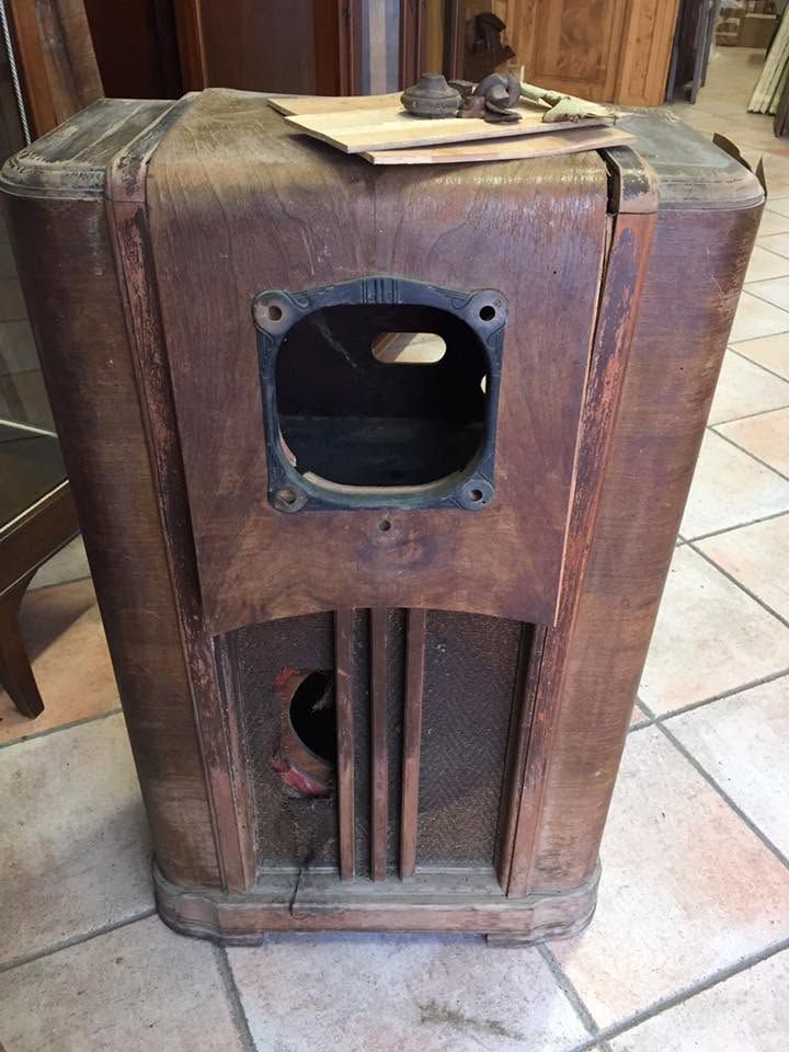 Vecchia cassa acustica in legno con aperture circolari su un pavimento piastrellato.