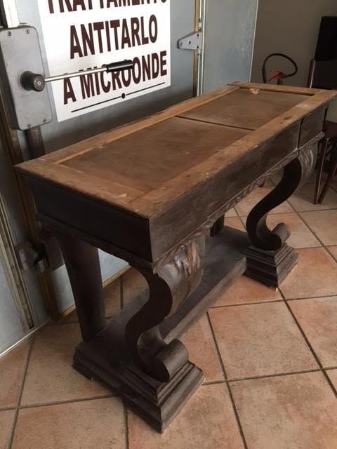Consolle in legno con gambe curve in una stanza piastrellata, accanto a un’insegna a parete.