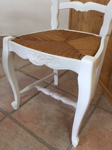 Sedia di legno bianco con seduta in paglia intrecciata su un pavimento piastrellato