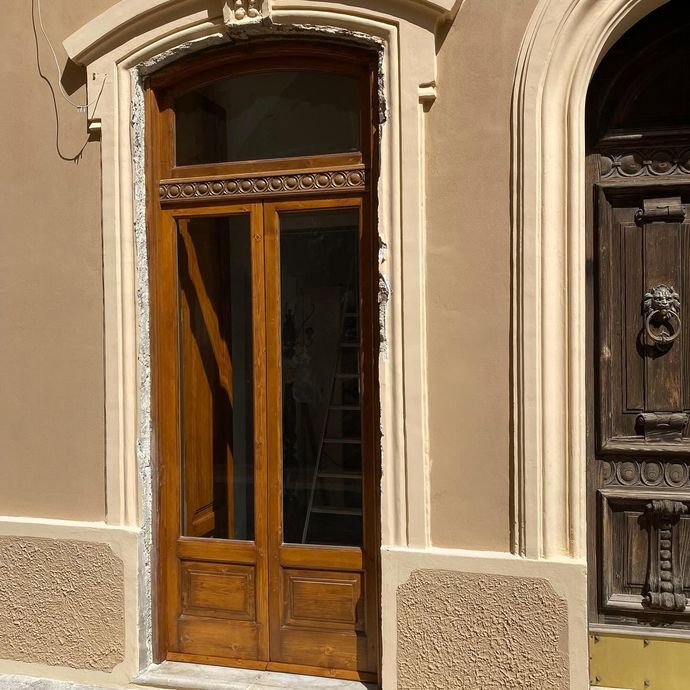 Porta in legno con pannelli in vetro, inserita in una facciata in stucco beige con cornice decorativa in pietra