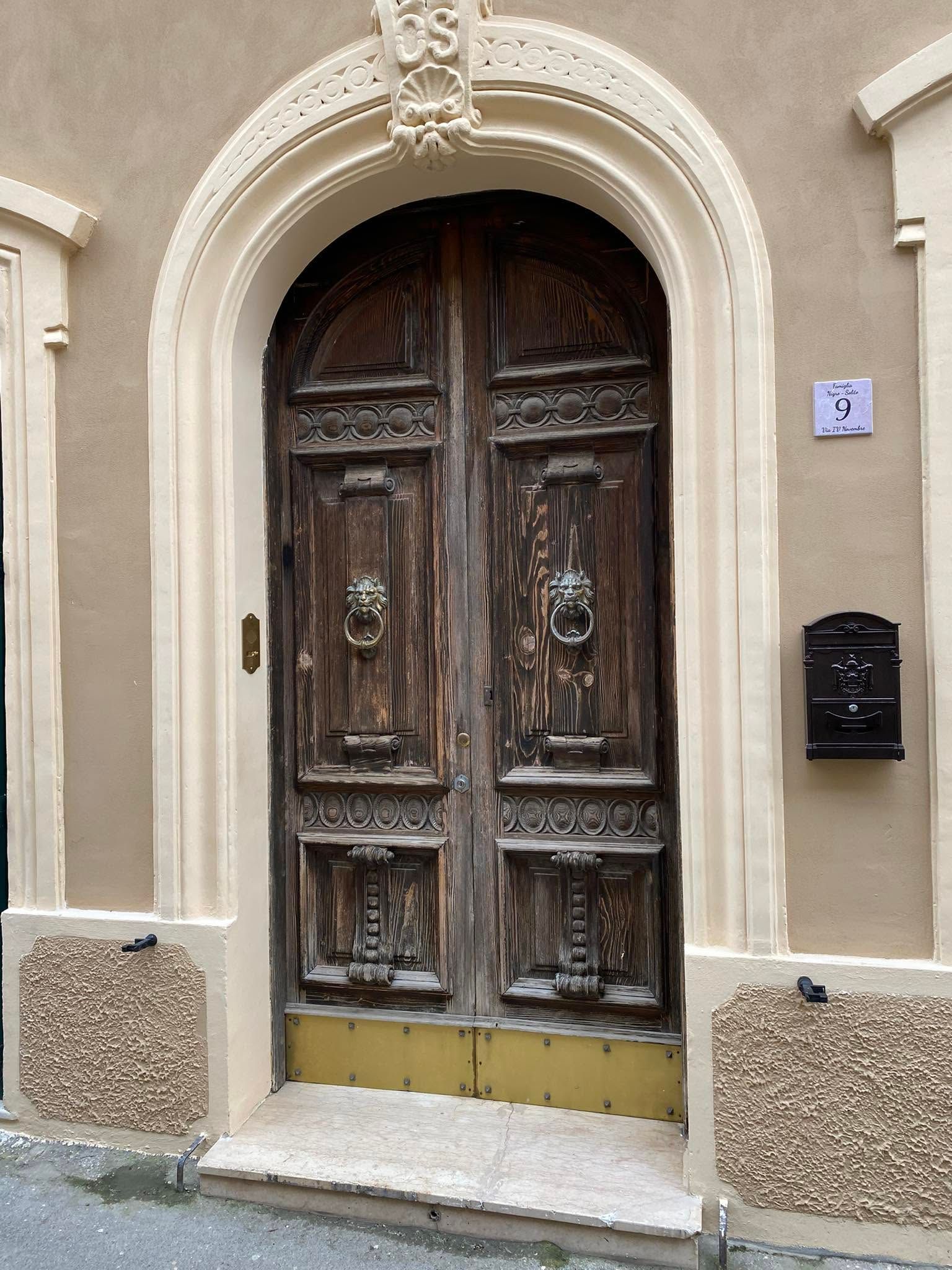 Ornata porta doppia in legno invecchiato, incastonata in un arco di pietra beige sulla facciata di un edificio