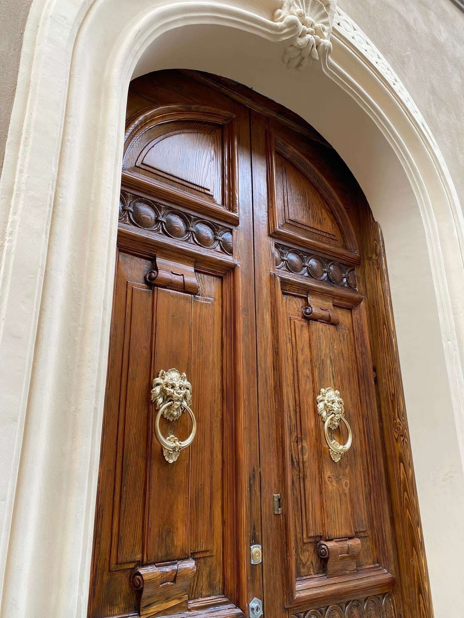 Elaborate porte doppie in legno con battenti in ottone, incastonate in un arco di pietra color crema