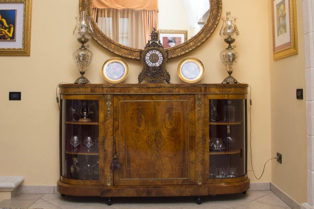Credenza in legno intagliato con ante in vetro, piatti e specchio in una stanza beige