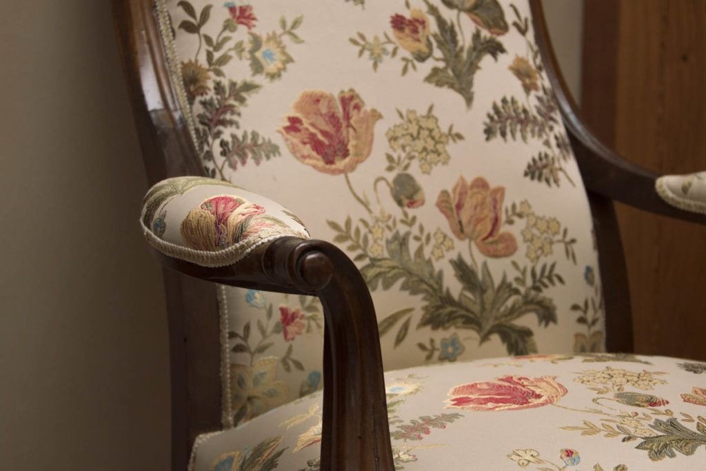 Poltrona imbottita a fiori con braccioli in legno e rivestimento color crema, in una stanza accogliente