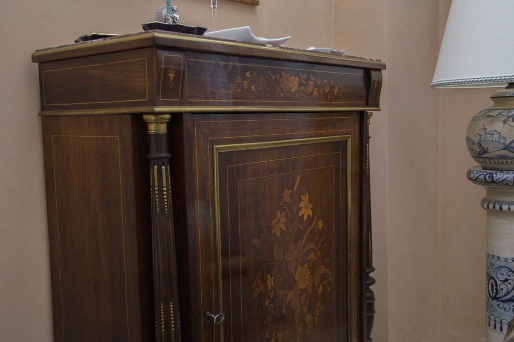 Antica credenza in legno scuro accanto a una lampada decorata, in una stanza dalla luce soffusa