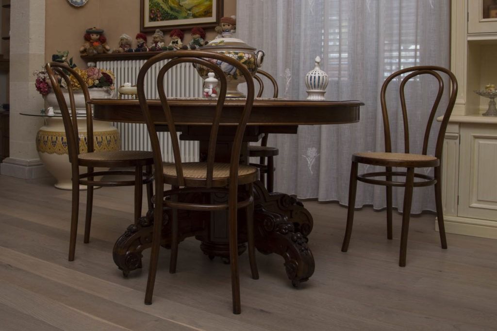 Sala da pranzo con tavolo e sedie in legno, centrotavola floreale e decorazioni artistiche alle pareti.
