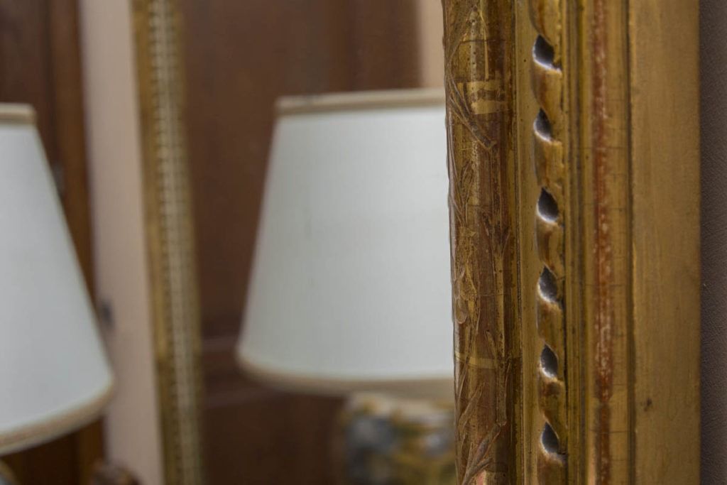 Primo piano di una cornice di specchio in legno con decorazioni a perline, che riflette un paralume bianco