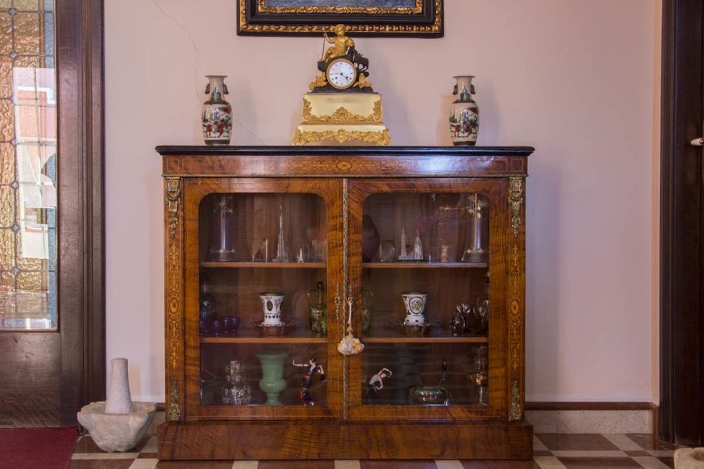 Credenza in legno con ante in vetro, vasi decorativi e un orologio in una stanza piastrellata