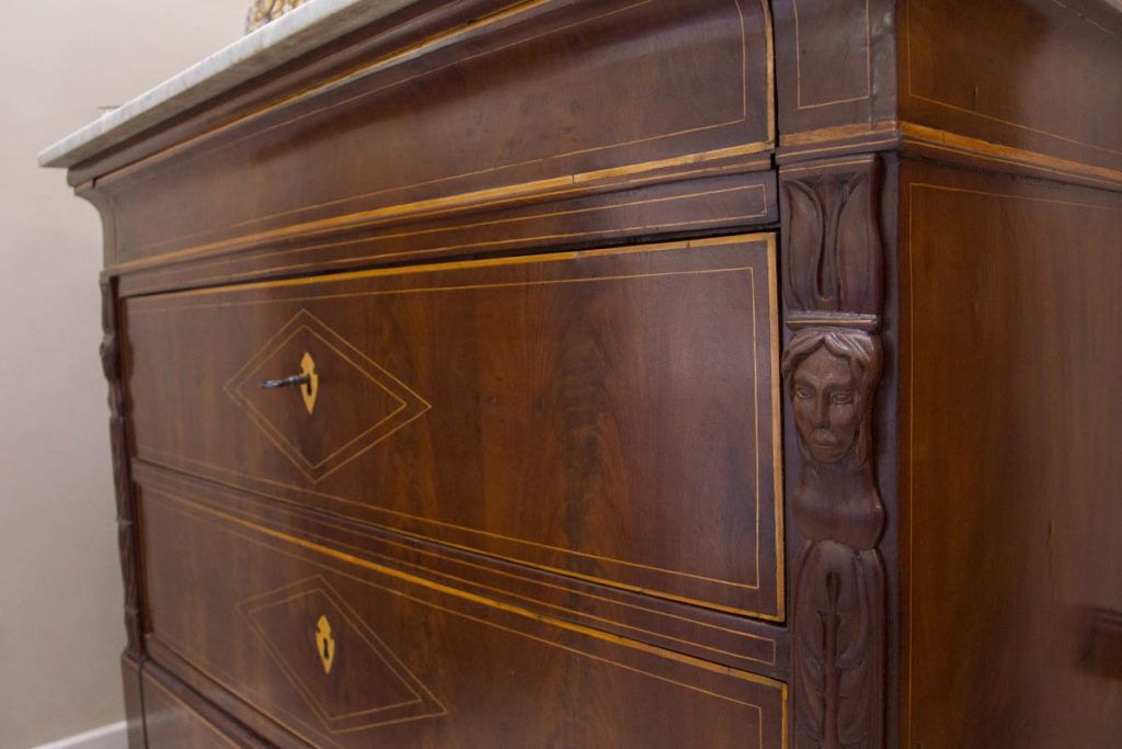 Primo piano di una cassettiera in legno scuro con maniglie in ottone e dettagli intagliati