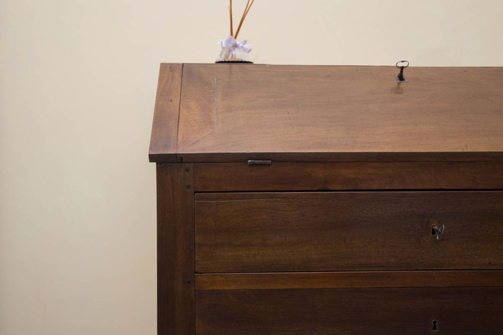 Cassettiera in legno con il piano marrone addossata a una parete beige, con un piccolo oggetto bianco che spunta dal bordo posteriore.