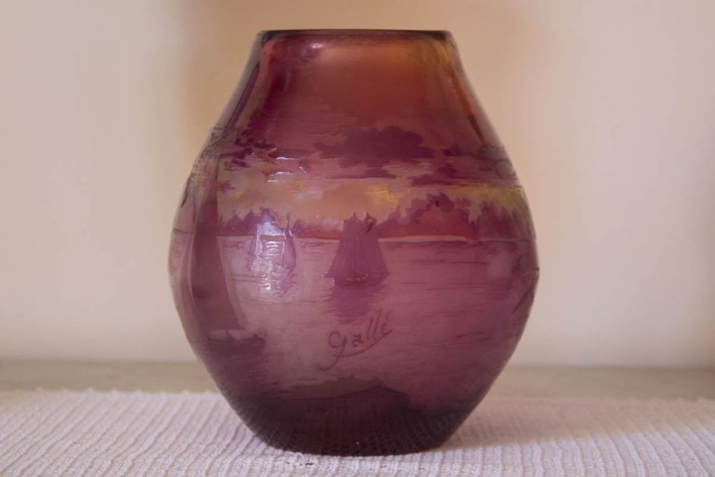 Vaso di vetro viola su una superficie bianca intrecciata, davanti a una parete beige