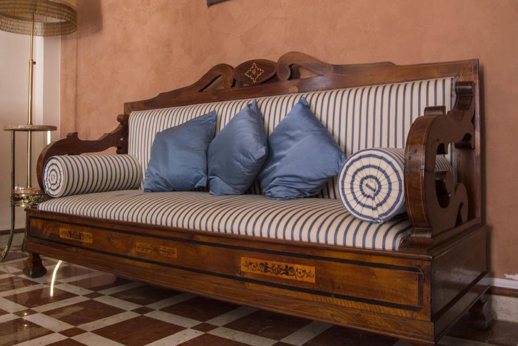 Divano in legno intagliato con rivestimento a righe e cuscini blu in un soggiorno