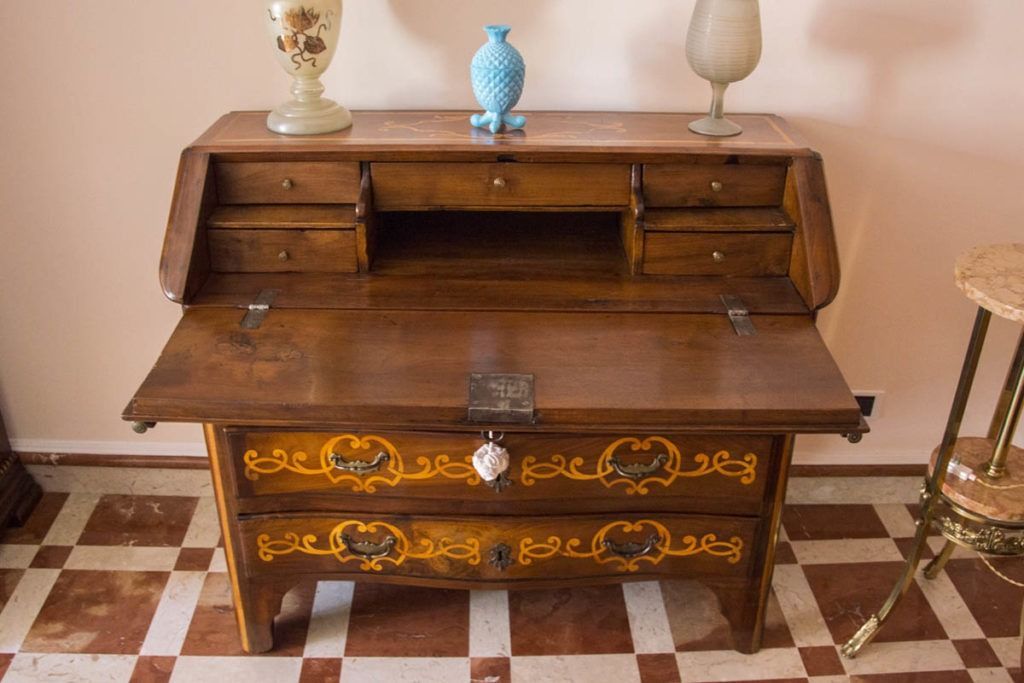 Scrivania antica in legno con raffinati dettagli dorati e vasi decorativi sopra, su un pavimento piastrellato.