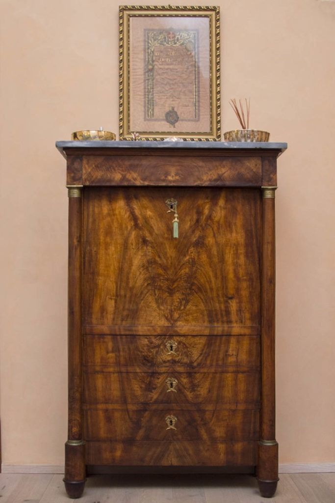 Mobile in legno intagliato con quadri incorniciati e piccoli oggetti decorativi sopra, contro una parete beige