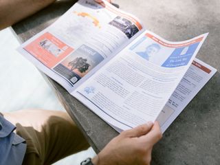 Person reading a magazine outdoors on a stone bench, with pages spread open in bright light