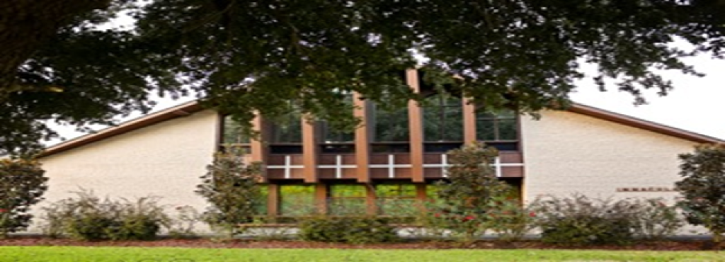 Front view of a white building with tall windows, framed by trees and greenery.
