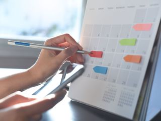 Hand placing a colored tab on a wall calendar, with a pen and phone nearby