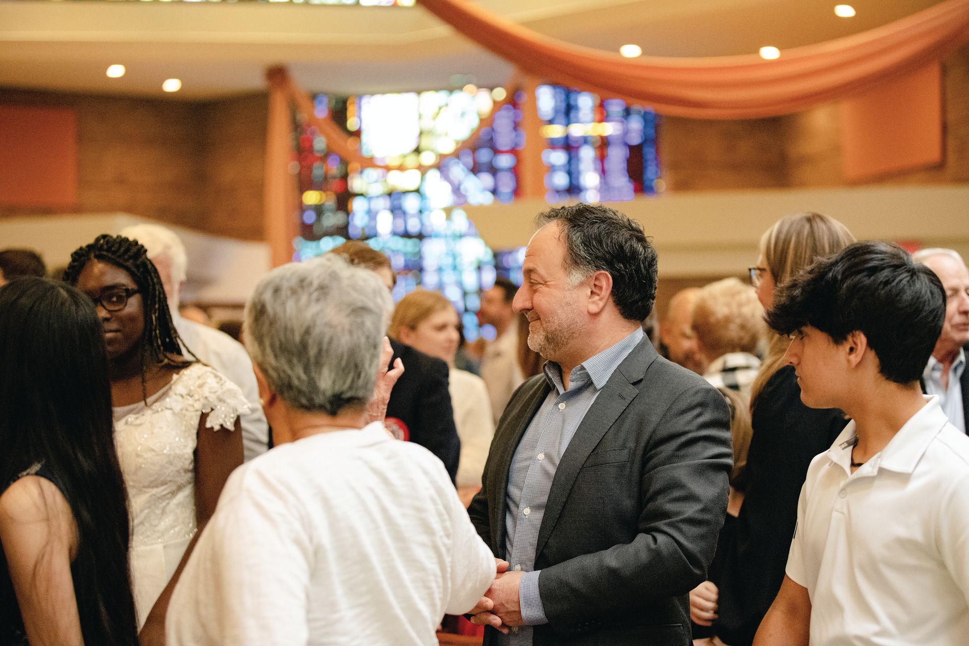 People conversing in a warmly lit church sanctuary with stained glass windows.
