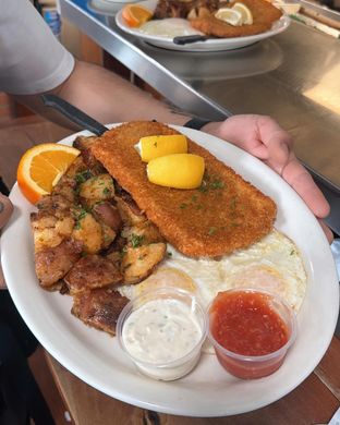 Plated seafood meal with fried fish, lemon wedges, orange slices, sauces, and fried eggs.