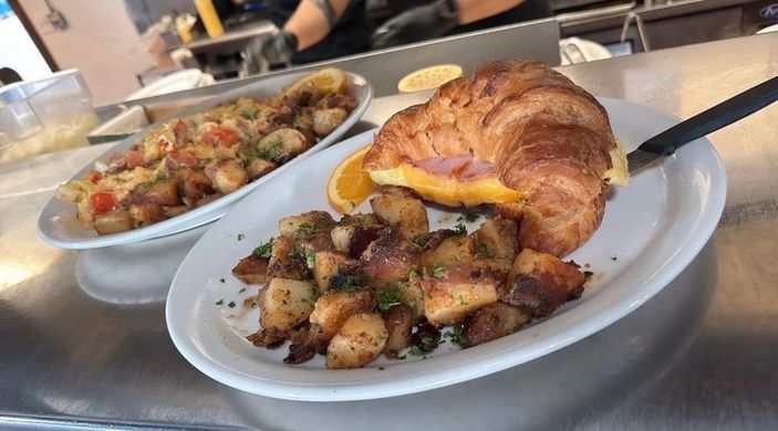 Breakfast plate with French toast, scrambled eggs, sausage, and syrup on a table.