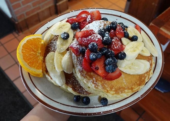 Plate of powdered sugar French toast topped with berries and a scoop of ice cream.