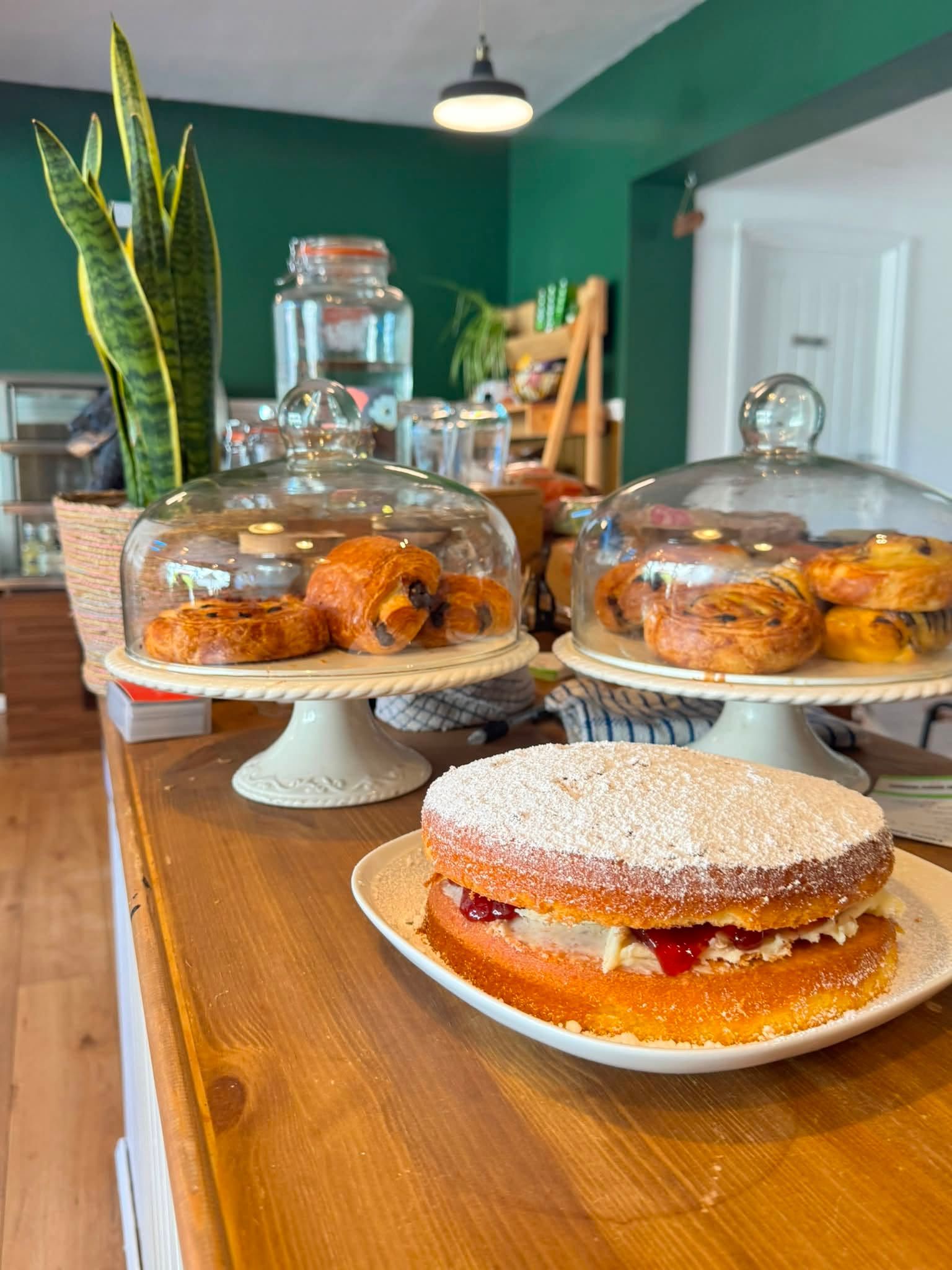 Pastries on white cake stands and under glass domes on a wooden table in a green cafe