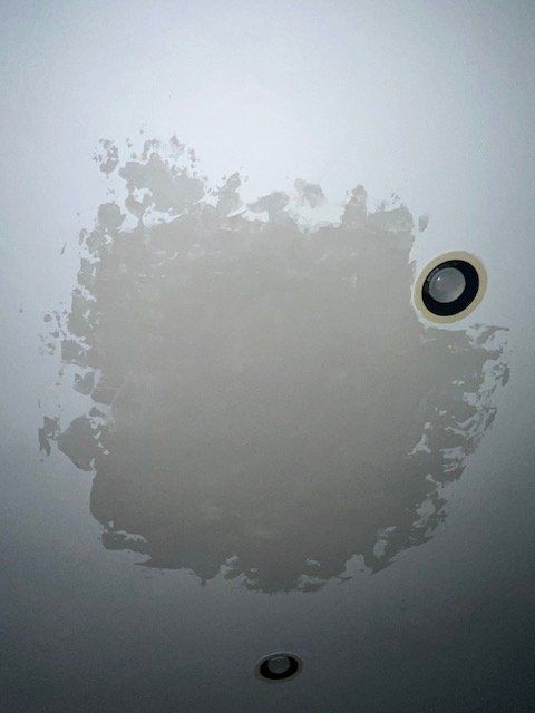 Ceiling with a large gray water stain near a recessed light and vent opening