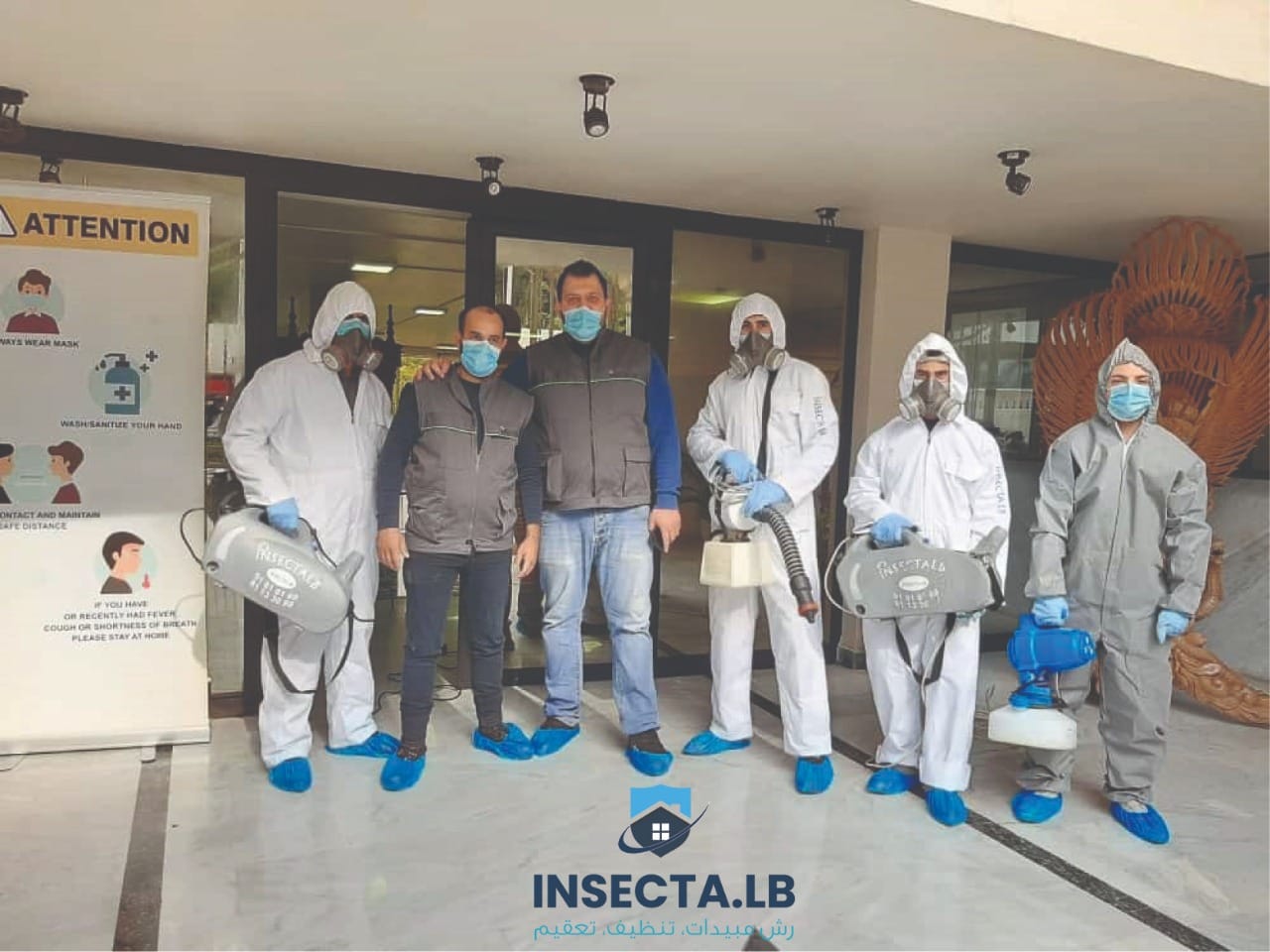 Group of men in protective suits, some with sprayers, posing with a sign that reads