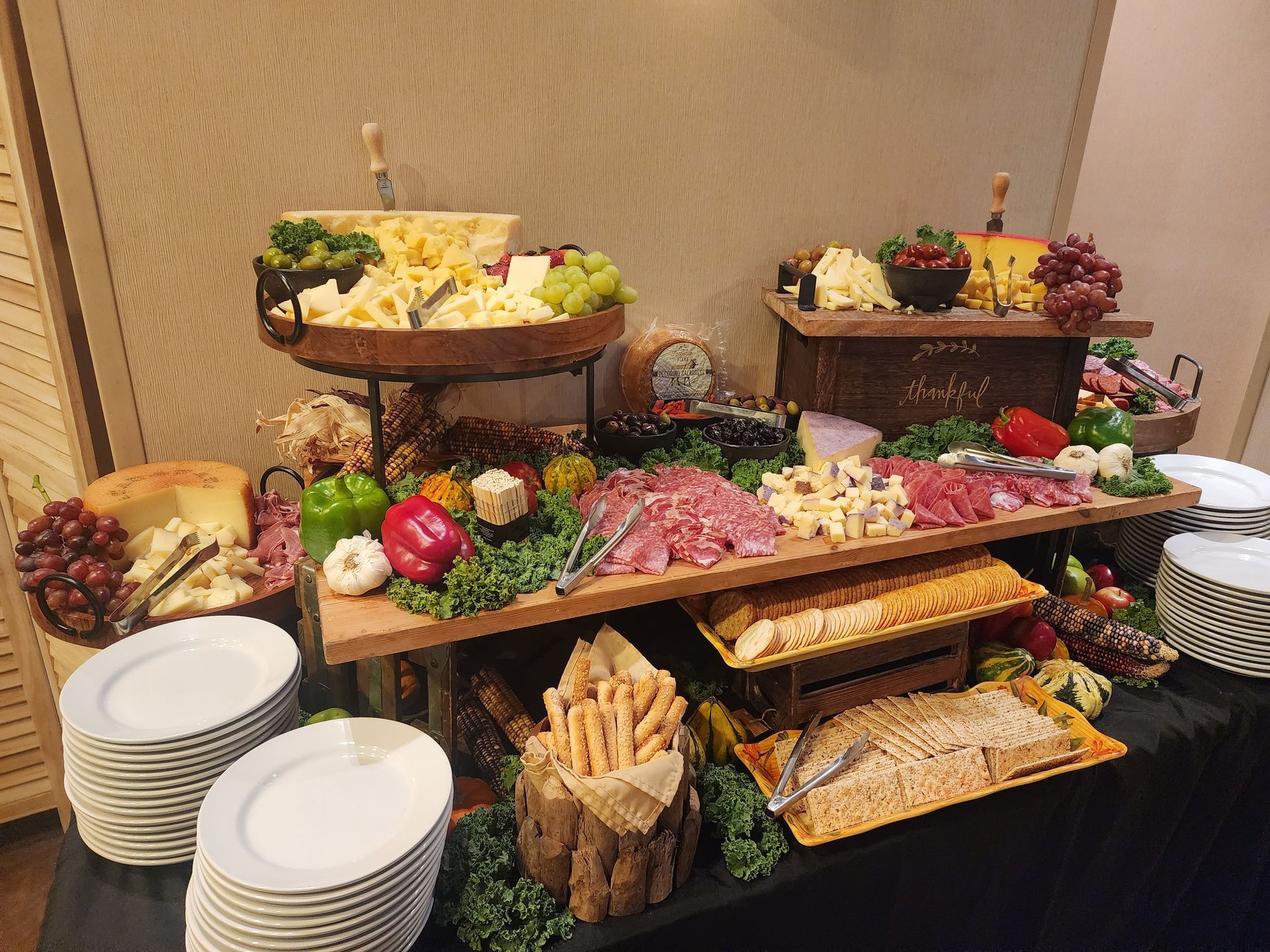 A buffet display featuring cheese, cured meats, crackers, grapes, and vegetables arranged on wooden risers and platters.