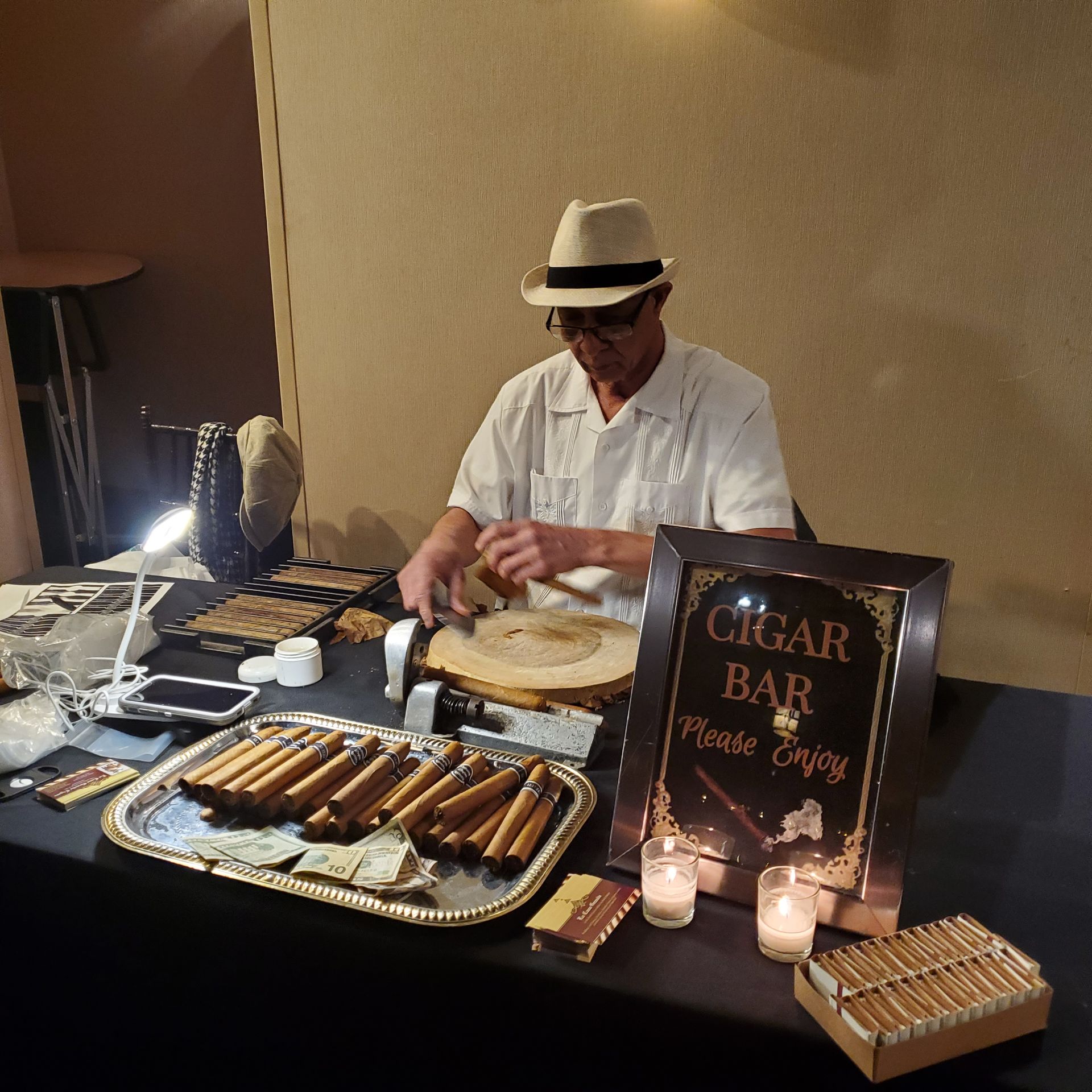 A person in a hat and white shirt prepares cigars at a 