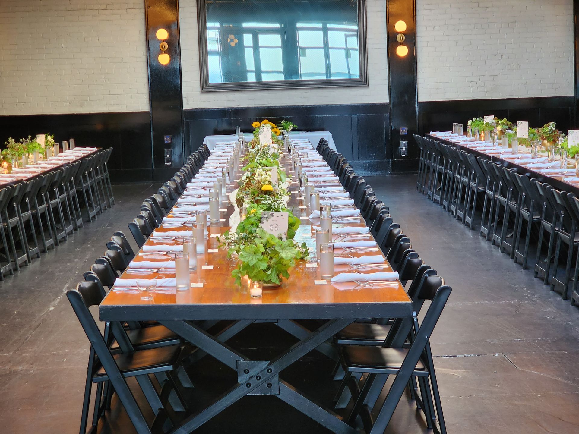 Long wooden banquet tables with green centerpieces set for a formal dinner in an elegant hall with dark accents.