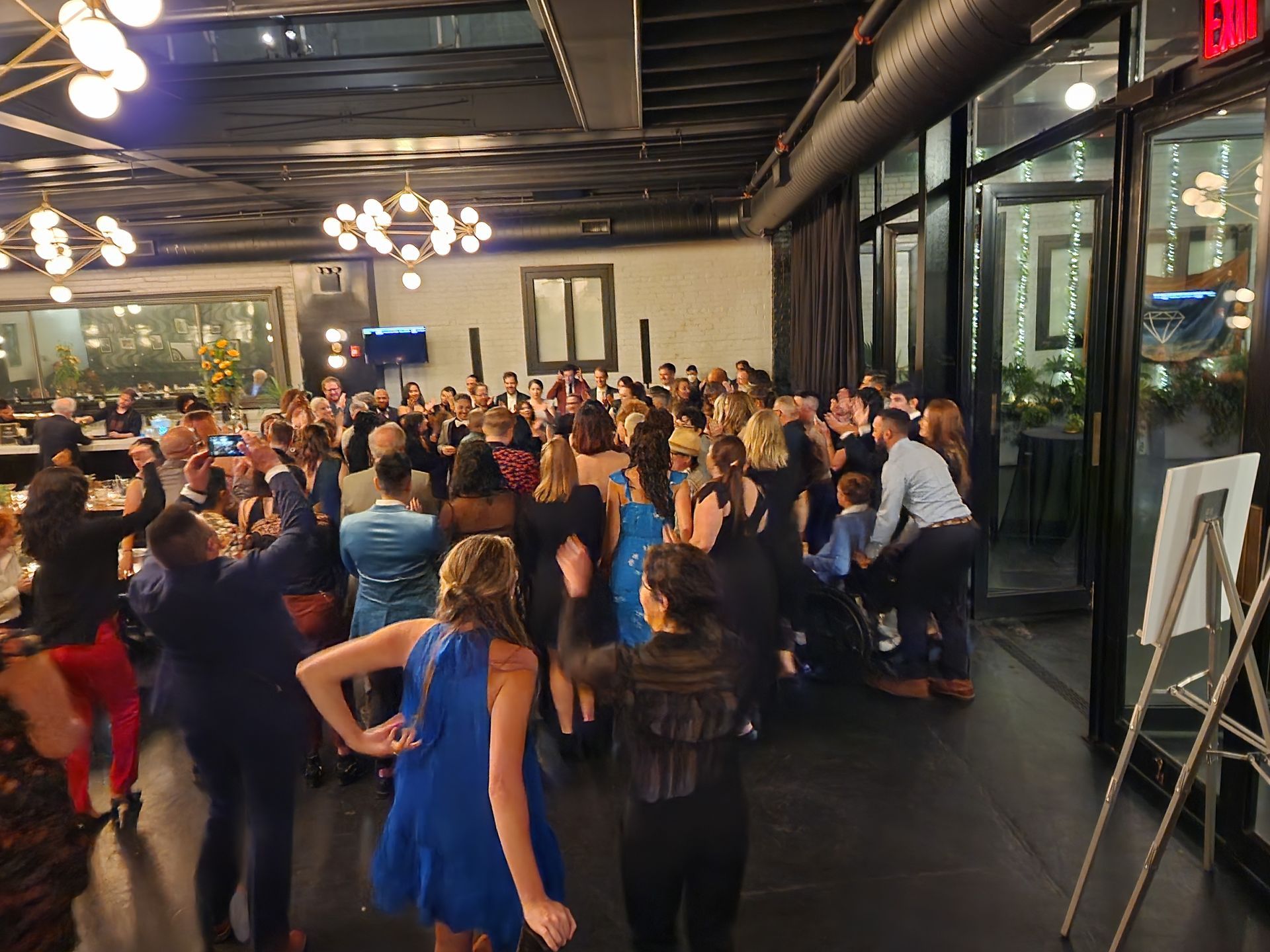 A crowded, dimly lit indoor event space where people are dancing and gathered in a lively party atmosphere.