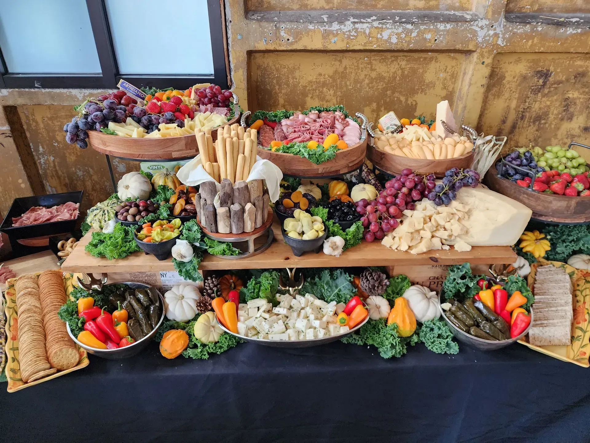 A large, elaborate charcuterie spread featuring an assortment of cheeses, meats, fruits, vegetables, and bread sticks.