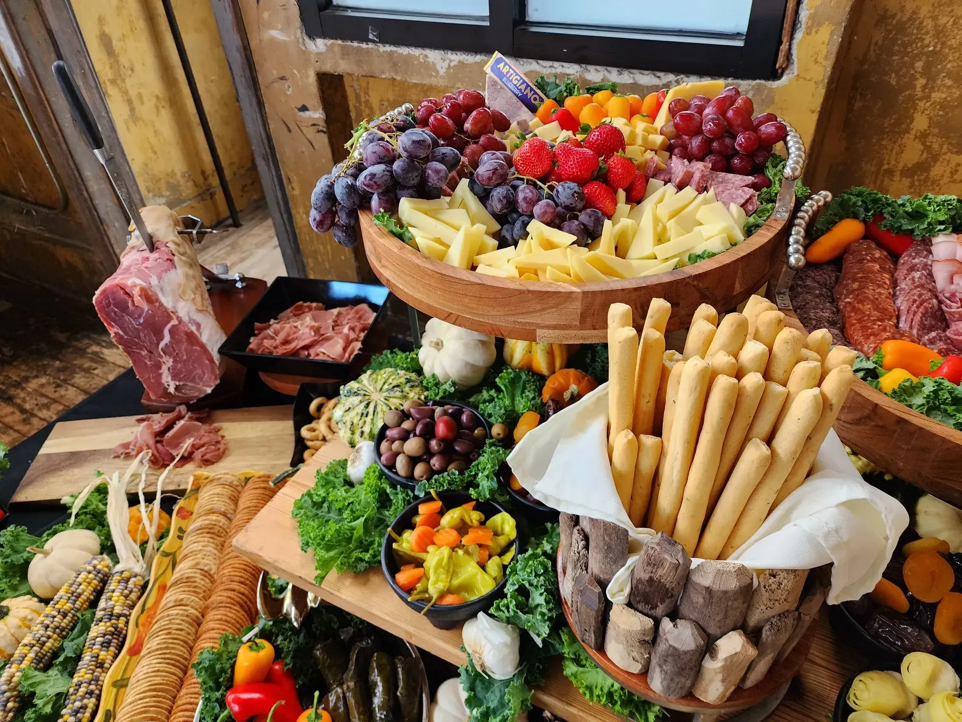 A lavish charcuterie spread featuring tiered wooden boards of cheeses, grapes, cured meats, breadsticks, and vegetables.